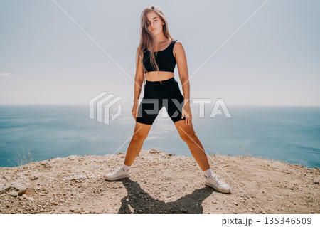 Woman in Black Sportswear Posing on Clifftop with Ocean View 135346509