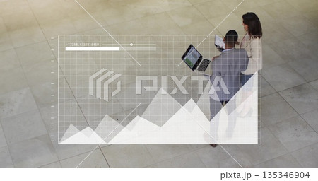 Two professionals wearing suits reviewing data overlay in lobby, with laptop, tablet, copy space 135346904