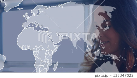 Standing woman wearing business casual inside office with world map overlay and blinds, copy space 135347022