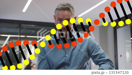 Gesturing man in blue shirt explaining DNA double helix graphic in office, with computer monitor Gesturing man in blue shirt explaining DNA double helix graphic in office, with computer monitor 135347120