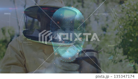 Examining beekeeper wearing suit and gloves observing hive frame in grove, with AR hologram 135347174