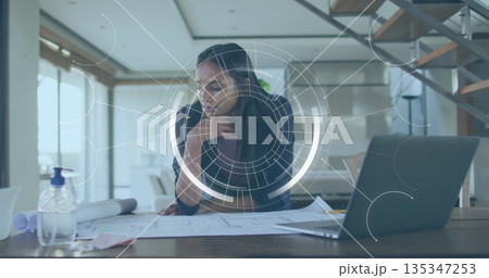 Reviewing female architect leaning over blueprints at modern home office, with sanitizer dispenser Reviewing female architect leaning over blueprints at modern home office, with sanitizer dispenser 135347253