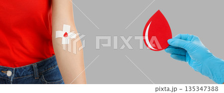 Donor with bandage and hand in glove hold decorative blood drop 135347388