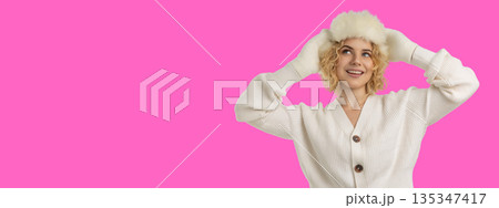 Woman wearing a fluffy hat smiles against a pink backdrop Woman wearing a fluffy hat smiles against a pink backdrop 135347417