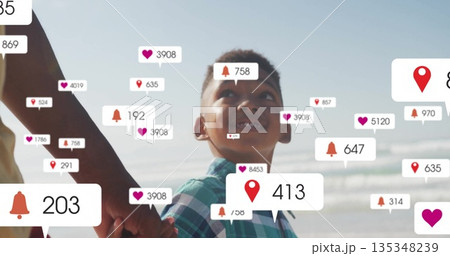 Walking father in yellow top son in green shirt holding hands on beach, floating notification icons 135348239