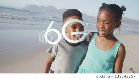 Smiling siblings wearing teal dress and gray t-shirt hugging on sandy beach, with 6G overlay 135348257