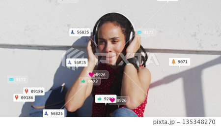Sitting woman pressing headphones to ears on patio ledge, with social media notifications 135348270