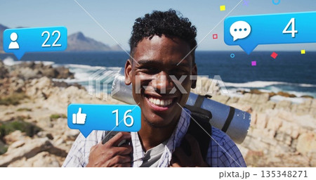 Smiling hiker wearing plaid shirt toting backpack with rolled mat on coast, social media overlays 135348271