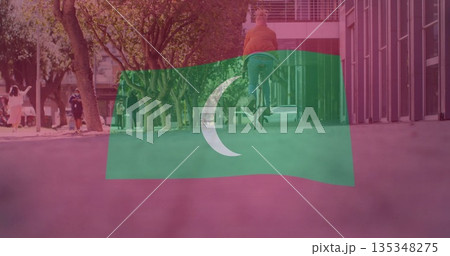 Riding cyclist wearing orange jacket along tree-lined pathway by glass facade, with flag overlay 135348275