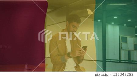 Leaning Hispanic man checking smartphone on mezzanine railing, tinted red yellow green glass panels 135348282