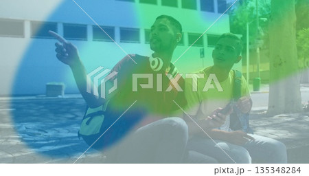 Pointing adult men sitting and looking left on bench at courtyard, with backpacks and headphones Pointing adult men sitting and looking left on bench at courtyard, with backpacks and headphones 135348284