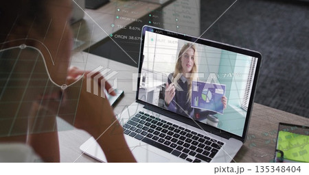 Watching presenter on laptop holding chart at office desk, with smartphone notepad pen coffee 135348404