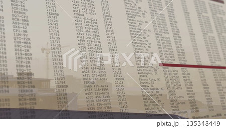 Displaying flight board showing codes and times on glass panel at airport, with building reflection 135348449
