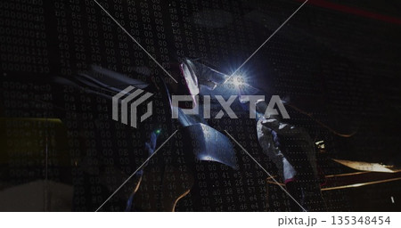 Female welder guiding torch in metal workshop, with glowing arc, helmet headlamp, code overlay 135348454