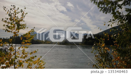Flowing river winding through mountain valley amid yellow trees, conifers, cloudy sky, 60 overlay Flowing river winding through mountain valley amid yellow trees, conifers, cloudy sky, 60 overlay 135348463
