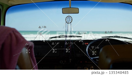 Framing camper van dash showing dreamcatcher hanging from rearview mirror facing beach, with towel 135348485