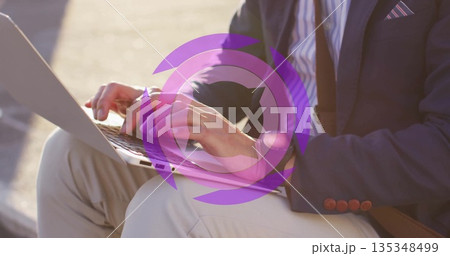 Typing man in business attire working on laptop on bench beside walkway, with leather bag strap Typing man in business attire working on laptop on bench beside walkway, with leather bag strap 135348499