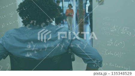 Pushing man in wheelchair down corridor, equations floating, coworker reading tablet, copy space 135348529