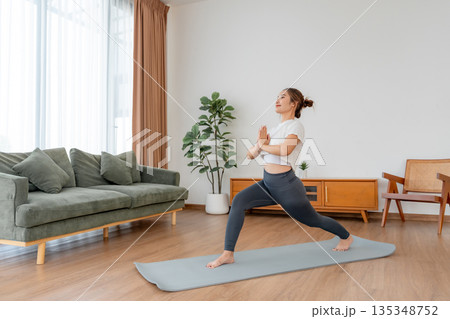 Happy young Asian woman practicing yoga and shoulder stretching  in living room at home 135348752