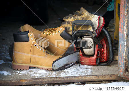 Work boots and chainsaw ready for winter outdoor labor, safety gear for cold weather jobs 135349074