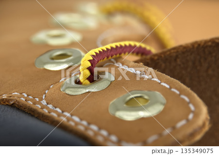 Close-up shot of a tan nubuck leather boot with yellow and maroon laces and metal eyelets Close-up shot of a tan nubuck leather boot with yellow and maroon laces and metal eyelets 135349075