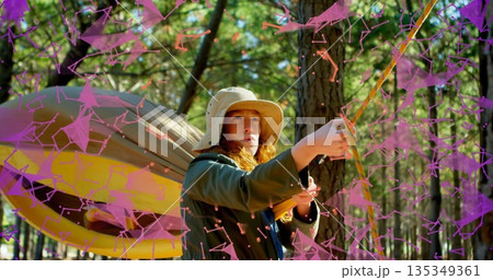 Woman wearing bucket hat and jacket tightening rope in forest, with hammock, purple digital overlay Woman wearing bucket hat and jacket tightening rope in forest, with hammock, purple digital overlay 135349361