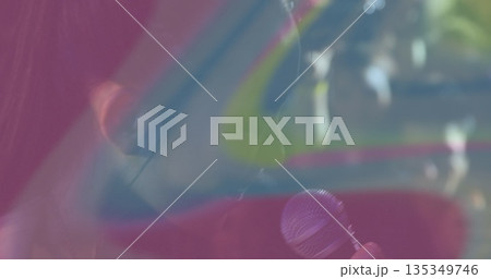 Singing performer holding microphone, wearing in ear monitor on stage with pink blue yellow panels 135349746