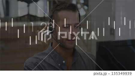 Monitoring agent wearing headset sitting at desk with screen in office, viewing overlay charts 135349939