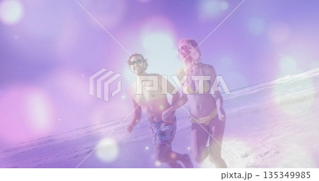 Running man and woman holding hands along shoreline at sunny beach, with sunglasses and swimwear 135349985
