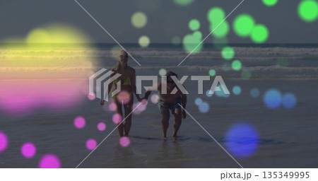 Running couple holding hands at beach shoreline, with yellow bikini, swim trunks and bokeh 135349995