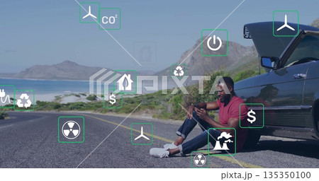 Checking man wearing red T-shirt holding smartphone on coastal road, open car hood, copy space 135350100