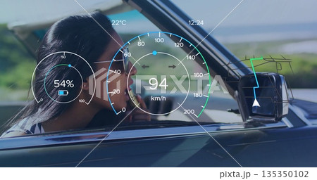 Applying lipstick Indian woman in aviator sunglasses driving convertible by coast, with HUD overlay 135350102