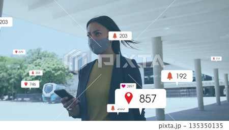 Standing Hispanic woman holding smartphone, wearing blazer and mask under canopy, viewing AR icons Standing Hispanic woman holding smartphone, wearing blazer and mask under canopy, viewing AR icons 135350135