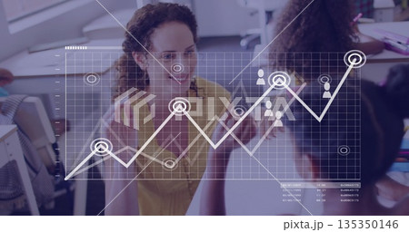 Gesturing teacher wearing yellow blouse teaching kids in classroom, with laptops and graph overlay 135350146