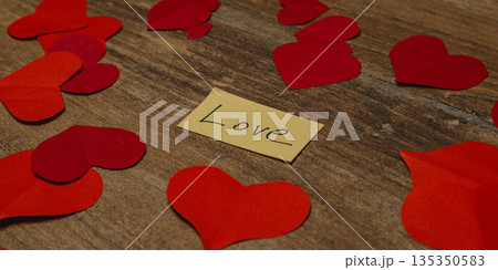 Hearts and message of love on a wooden table surrounded by paper cutouts 135350583