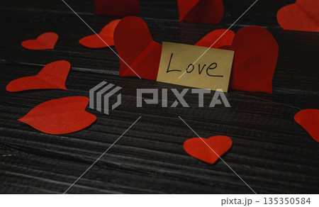 Decorative red hearts and a note saying love on a black wooden table Decorative red hearts and a note saying love on a black wooden table 135350584