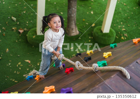child girl using a rope to climb up a wooden slope at outdoor playground child girl using a rope to climb up a wooden slope at outdoor playground 135350612