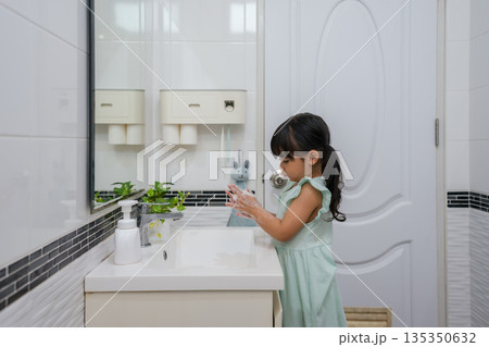 child girl washing her hands with soap in bathroom sink for hygiene 135350632