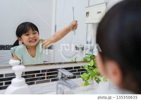 girl child brushing teeth at reflection in mirror in bathroom 135350635