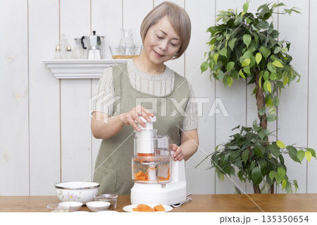 キッチンでフードプロセッサーを使い料理をするシニア女性 135350654