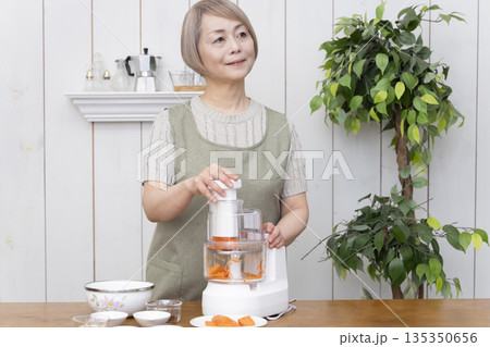 キッチンでフードプロセッサーを使い料理をするシニア女性 135350656