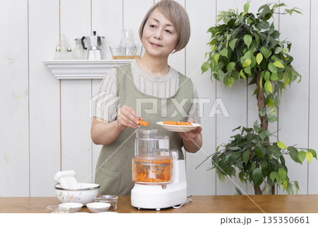 キッチンでフードプロセッサーを使い料理をするシニア女性 135350661