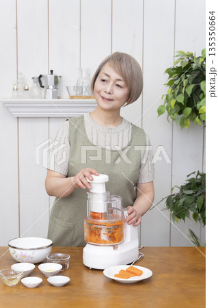 キッチンでフードプロセッサーを使い料理をするシニア女性 135350664