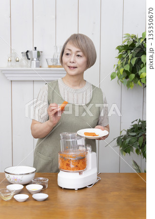 キッチンでフードプロセッサーを使い料理をするシニア女性 135350670