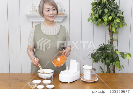 キッチンでフードプロセッサーを使い料理をするシニア女性 135350677