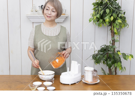 キッチンでフードプロセッサーを使い料理をするシニア女性 135350678