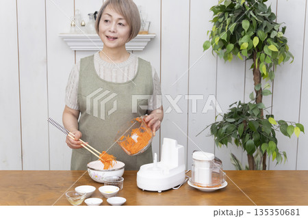 キッチンでフードプロセッサーを使い料理をするシニア女性 135350681