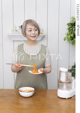 キッチンでフードプロセッサーを使い料理をするシニア女性 135350711