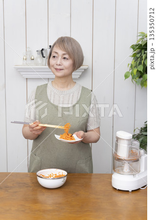 キッチンでフードプロセッサーを使い料理をするシニア女性 135350712