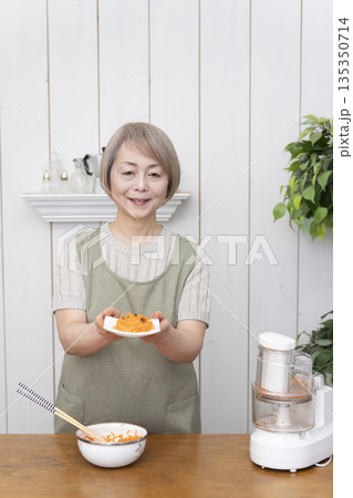 キッチンでフードプロセッサーを使い料理をするシニア女性 135350714